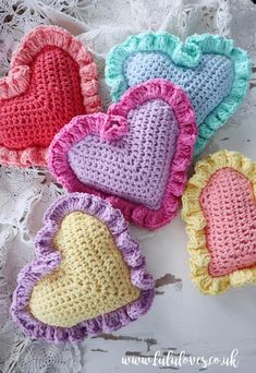 four crocheted hearts sitting on top of a white doily next to each other