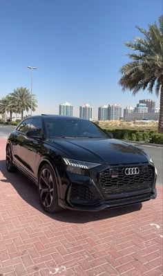 a black car parked in front of palm trees on a brick road with buildings in the background