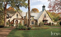 a stone house with a clock tower on the roof and trees in front of it