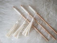 three wooden knitting needles are laying on a white furnishing with four tassels