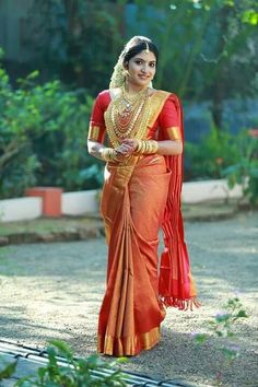 a woman in an orange sari and gold jewelry is walking down the street with her hand on her hip