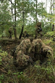 some soldiers are in the woods with their camouflage gear and helmets on, while one soldier is laying down