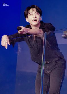 a young man standing on top of a stage holding onto a glass railing with his hand