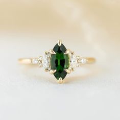 an oval cut green and white diamond ring with three smaller diamonds around the band on a beige background