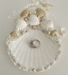 a ring sits on top of a shell with pearls and seashells around it