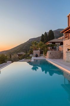 an empty swimming pool in front of a house with mountains in the background at sunset