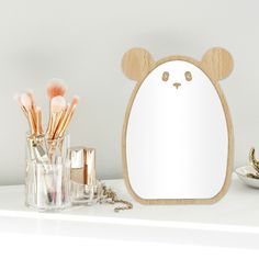 a bear shaped mirror sitting on top of a white counter next to makeup brushes and other items