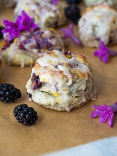 the muffins are covered with icing and blackberries on the table next to flowers