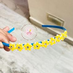 a hand holding a yellow and blue headband that has flowers on it, with the bottom beaded