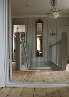 an open door leading to a hallway with chandelier and mirror on the wall