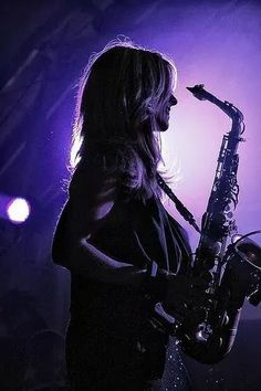 a woman playing the saxophone on stage at a music concert with purple lighting behind her