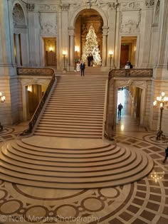 an ornate staircase in the middle of a building with people walking down it and christmas trees on either side