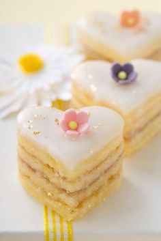 three small heart shaped cakes with flowers on them sitting on a white plate next to a yellow ribbon