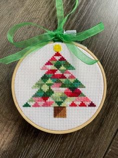 a cross stitch christmas tree ornament hanging on a wooden table with green ribbon