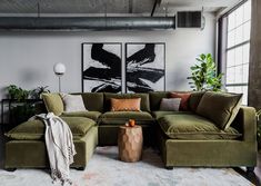 a living room with green couches and art on the wall behind them, along with potted plants