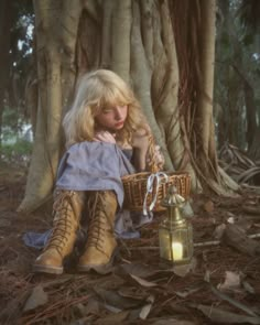 a woman sitting in the woods next to a lantern