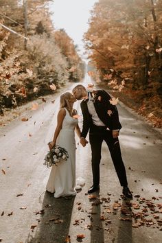 a newly married couple standing on the side of a road surrounded by leaves and trees