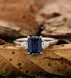 a blue and white diamond ring sitting on top of a leaf covered ground in the grass