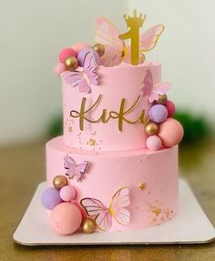 a pink and gold cake with butterflies on it's top, sitting on a white plate