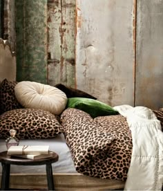 a leopard print comforter on a bed with green pillows and a white blanket in front of an old wooden wall