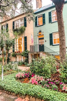 an old building with many windows and green shutters on the front, surrounded by flowers and trees