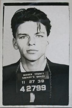 this is an old mug shot of a young man with his hair tied back and wearing a chain around his neck