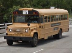 a yellow school bus driving down a road next to a fence and trees in the background