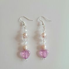 two heart shaped glass beads hanging from silver earwires on a white table top