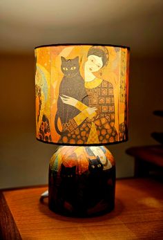 a lamp that is sitting on top of a wooden table next to a cat painting