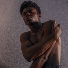 a shirtless man with his arms crossed posing for a photo in front of a wall