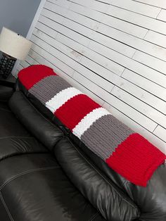 a black leather couch with a red, white and grey knitted pillow on it