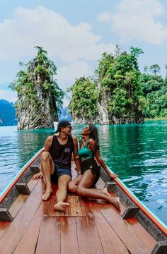 two people sitting on the back of a boat in front of some trees and water