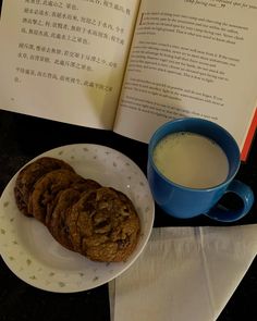 an open book next to a plate with cookies and a cup of milk on it