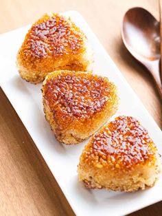 three pieces of breaded pastries on a white plate with spoons next to it