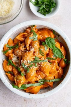 a white bowl filled with pasta covered in sauce and garnished with fresh herbs