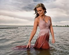 a woman in a pink dress standing in the water with her hands on her hip