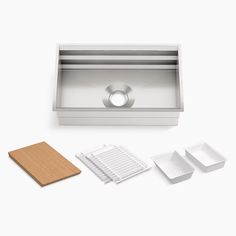 a stainless steel kitchen sink and accessories on a white surface with a wooden cutting board