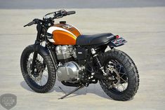 an orange and white motorcycle parked on top of a cement road next to a parking lot