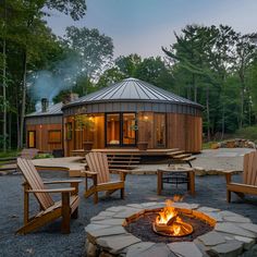 Discover a cozy modern Nordic yurt retreat nestled in a tranquil forest. This stylish yurt features a wooden exterior, sleek metal roof, and large windows that emit a warm interior glow. A circular stone fire pit surrounded by Adirondack chairs creates a perfect outdoor seating area for evenings under the stars. The lush greenery and serene ambiance make this yurt an ideal escape into nature. Luxury Yurt Interior, Yurt Architecture, Yurt Retreat, Round House Plans, Grass Roof, Forest Setting