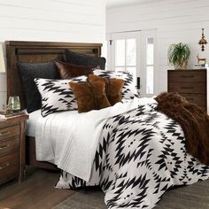 a bed with black and white comforter in a bedroom next to a dresser, mirror and lamp