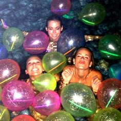 three women are in the water surrounded by large, colorful balls and streamers that look like they're floating