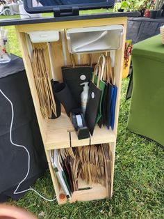 a wooden shelf filled with assorted items sitting on top of a grass covered field