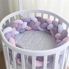 a white crib with pink, purple and grey pillows in it's center