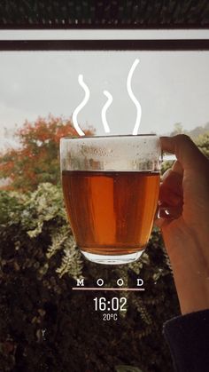 a person holding a cup of tea in front of a window with the words good morning on it