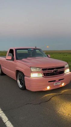 a pink pick up truck parked on the side of the road in front of an open field