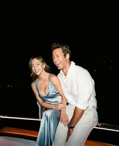 a man standing next to a woman on top of a boat in the ocean at night