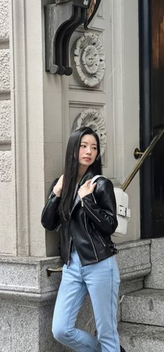 a woman in black jacket and jeans leaning against the wall with her hand on her hip