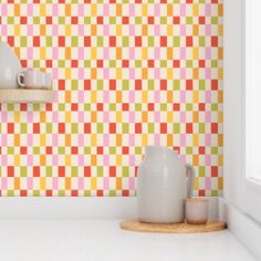 a kitchen counter topped with two white vases next to a wall covered in multicolored tiles