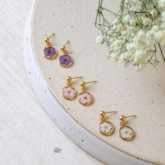 three pairs of earrings sitting on top of a white table next to flowers and branches