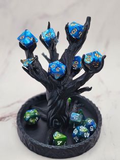 a small tree with blue and yellow dice on it's branches in front of a marble background